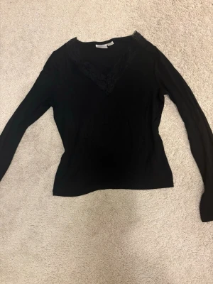 Svart stickad tröja med spetsdetalj - Säljer en svart stickad tröja från Gina Tricot med snygg V-ringning och spetsdetalj vid halsen. Tröjan har långa ärmar och är perfekt för dig som gillar en enkel men ändå trendig look.