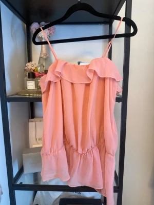 Ljusrosa volangtop med smala band - Supersöt ljusrosa topp med tunna justerbara axelband och volangdetaljer upptill. Toppen har en luftig passform och är tillverkad i ett lätt, skirt material som ger en romantisk vibe. 