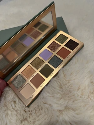 Ögonskuggspalett Anastasia Beverly Hills - Snygg ögonskuggspalett från Anastasia Beverly Hills med 12 nyanser i grönt, lila, brunt, guld och beige. Paletten har både matta och skimriga skuggor och kommer i ett stilrent grönt fodral med spegel. Perfekt för kreativa och trendiga ögonlooks.