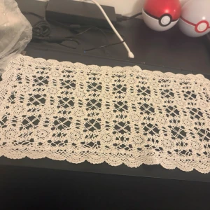 Vitt virkat bordsunderlägg - Säljer ett rektangulärt vitt virkat bordsunderlägg med detaljerat blommönster och vågig kant. Perfekt som dekoration på bord eller byrå. Materialet är tunt garn i bomull och mönstret är klassiskt och handgjort.