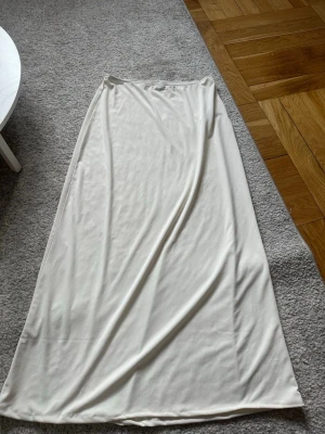 Vit långkjol från Gina Tricot - Säljer en stilren vit långkjol från Gina Tricot. Kjolen har en enkel och rak passform med mjukt, lätt material som ger ett snyggt fall. Perfekt att matcha med crop tops eller stickade tröjor för en clean look.