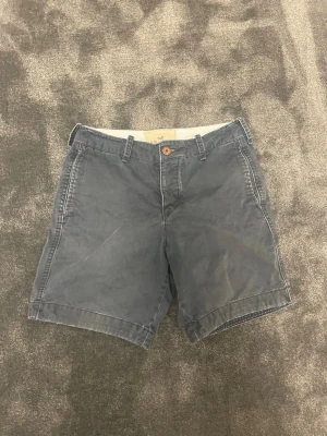 Hollister shorts - Säljer ett par klassiska blå shorts från Hollister med normal passform och midwaist. Shortsens material är mjuk bomull och de har fickor både fram och bak samt en diskret logga på baksidan. Perfekta för sommarens alla äventyr.