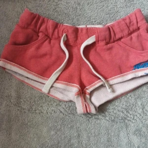 Lågmidjade shorts - Säljer ett par lågmidjade minishorts från Superdry i storleken xs💓💓. De är korall/röda. 