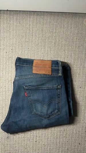 Blå Levi's 511 slim jeans - Säljer ett par klassiska blå Levi's 511 slim jeans med fem fickor och snygga kontrastsömmar. Jeansen har en ikonisk läderpatch bak i midjan och den röda Levi's-taggen på bakfickan. Tillverkade i slitstarkt denimtyg, perfekta för en avslappnad look. 