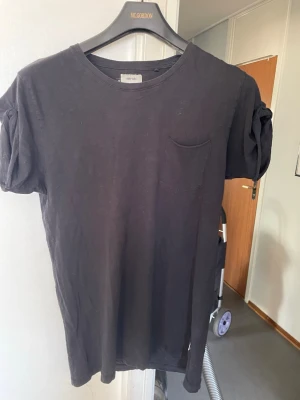 Svart t-shirt med ficka från Win win - En svart t-shirt från win win  i mjuk bomull. T-shirten har rund halsringning, korta ärmar med lätt puff och en liten bröstficka. Enkel och clean design som passar till det mesta.