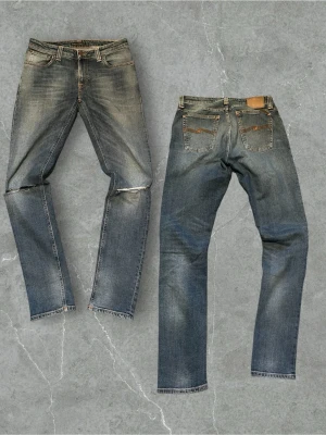 Feta Nudie Jeans - Säljer ett par blå jeans från Nudie Jeans med snyggt slitna detaljer och klassisk femficksmodell. Jeansen har raka ben, orange kontrastsömmar och en patch bak i midjan. Materialet är denim i bomull och tvätten ger en cool vintagekänsla.