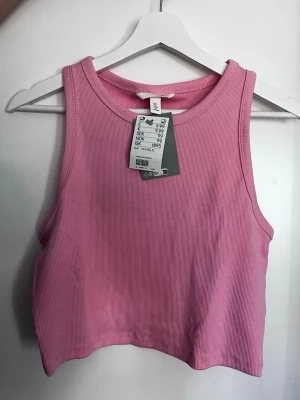 Rosa ribbad croppad linnetopp H&M - Säljer en rosa ribbad croppad linnetopp från H&M. Toppen är ärmlös med rund halsringning och har en enkel, stilren design som passar perfekt till jeans eller kjol. Materialet är mjukt och stretchigt för en bekväm passform.