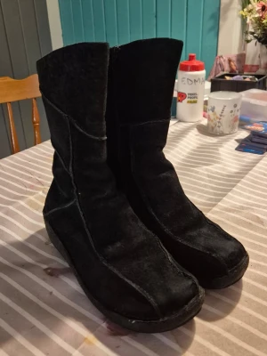 Svarta mockastövlar - Säljer ett par svarta stövlar i mocka med markerade sömmar. Stövlarna har en något rundad tå och dragkedja på insidan för enkel påtagning. Perfekta för dig som vill ha en stilren och bekväm look. 