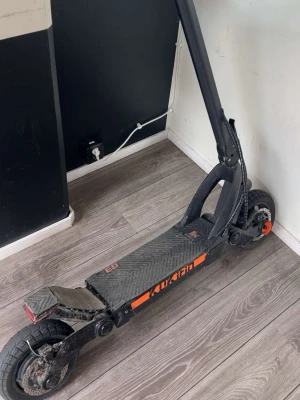 Svart elscooter KuKirin G3 - Säljer en svart elscooter av modellen KuKirin G3 med digital display och orangea detaljer. Scootern har bred fotplatta med halkskydd, stora luftfyllda däck och robust ram i metall. Perfekt för snabba transporter i stan.