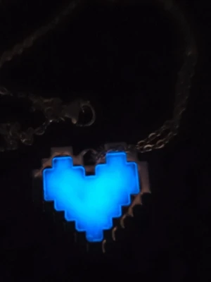 Glow in the dark pixelhjärta halsband i rostfritt stål  - Unikt halsband med ett blått, självlysande pixelhjärta som hänge. Hjärtat har en tydlig retro gaming-vibe och sitter på en tunn metallkedja. Perfekt för dig som gillar gaming eller vill ha något som verkligen sticker ut i mörkret. Tål vatten och missfärgas inte. Lång livslängd. 