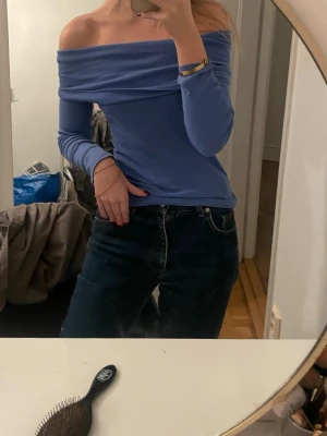 Blå offshoulder topp - Säljer en snygg blå offshoulder topp med långa ärmar. Toppen har en bred kant upptill som ger en cool och trendig look. Perfekt att styla med jeans eller kjol för en chill vibe. (En sömm har lossat där bak, det är under off shouldern så inget som syns,  går också att sy ihop enkelt)