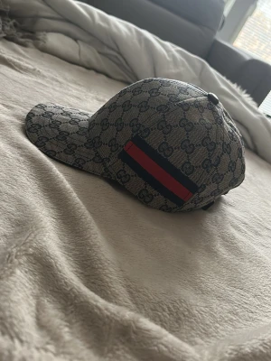 Fin keps  - Säljer en stilren keps i beige/brun monogram-design med klassiskt mönster över hela. Har en snygg röd/grön rand på sidan som ger en exklusiv look.  Kepsen har böjd skärm och justerbar passform baktill så den passar de flesta. Perfekt till både streetwear och clean outfits.  Skick: Bra skick (se bilder)   Storlek: One size (justerbar)  Hör av dig vid frågor eller fler bilder ✌️