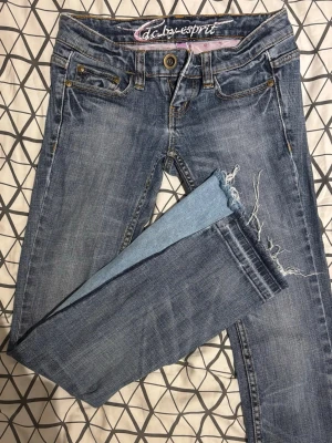 Blå jeans från Esprit - Säljer ett par blå jeans från Esprit med slitningar och rå kant vid benslutet. Jeansen har klassisk femficksmodell, synliga sömmar i kontrastfärg och knappgylf. Perfekta för en avslappnad och trendig look. Dom är omsydda vid bena, då det var skinnyjeans till en början. Säljer pågrund av att dom är för korta.