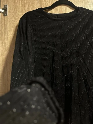 Svart glittrig tröja  från ONLY - Snygg svart  tröja från ONLY med tunna vertikala glittriga ränder. Tröjan  har rund halsringning och långa ärmar. Materialet känns mjukt och stretchigt, perfekt för dig som vill sticka ut lite extra.