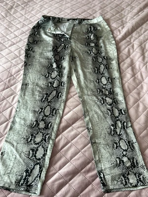 Ormmönstrade raka silke byxor - Säljer ett par snygga raka byxor med ormmönster i svart och grått. Byxor har hög midja och klassisk femficksmodell. Materialet känns mjukt  perfekt för dig som vill sticka ut med en trendig look.