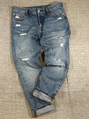Levi’s 501 CT Distressed Tapered W29 💙✨ - Levi’s 501 CT distressed denim. Mid blue wash with strong fading and factory-style rips. Relaxed top block with a clean tapered leg. Perfect everyday denim with character. Tag W29 L34 but runs bigger — check measurements.  Attention: Worn and used. Distressing and fading are intentional. Review photos carefully before buying.  Measurements (flat): Waist 44 cm Rise 25 cm Thigh 30 cm Inseam 72 cm  Good used condition. No major flaws.