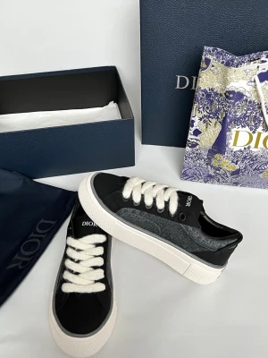 Svarta Dior sneakers med monogram - Snygga svarta Dior sneakers med vit sula och tjocka vita skosnören. Sidan har det klassiska Dior-monogrammet i grått och svart, och ovandelen är i en mix av textil och läder. Perfekta för dig som vill ha en exklusiv och trendig look.