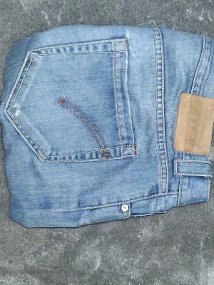 Dondup jeans - Säljer ett par ljusblå jeans i klassisk modell, tillverkade i Italien av 100% bomull. Jeansen har en bakficka med kontrastsöm och en läderpatch i midjan. Perfekta för dig som gillar tidlös denimstil.