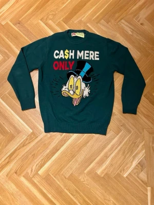 MC2 Saint Barth tröja stickad  - Säljer en mörkgrön stickad tröja från MC2 Saint Barth med tryck av Joakim von Anka och texten 'CASH MERE ONLY' i vitt, rött och gult. Väldigt sällsynt, Perfekt skick, storlek M