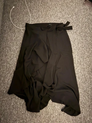 Svart omlottkjol med knytband - Snygg svart omlottkjol med knytband i midjan, aldrig använd och säljes i storlek S 