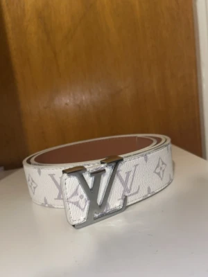 Svart och vitt bälte - Snyggt vitt med klassiskt monogrammönster i grått och silverfärgat spänne. Bältet är tillverkat i slätt läder och har en brun baksida. Perfekt accessoar för att lyfta din outfit.