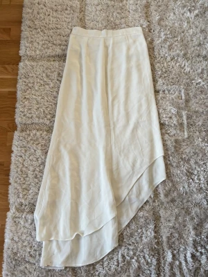 Vit långkjol  - Säljer en elegant vit långkjol med omlott-design. Sitter snyggt på. Finns små fläckar längst ner. 