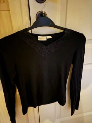 Blå långärmad topp med spets - Blå långärmad topp med v-ringning och dekorativ spetsdetalj vid halsen. Tunn och mjuk i materialet, perfekt för lager på lager eller som den är. Enkel och stilren design som passar till mycket.