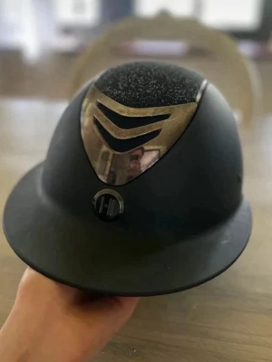 Svart ridhjälm från One k  - Stilren svart ridhjälm från One k med glittrig ovansida och metallfärgad detalj framtill. Hjälmen har bred skärm och ventilerande design. Storlek 0 i skalet, och 53-54 i liner som går att byta ut. Mips hjälm. Ny pris är 5200kr men jag säljer för 3500kr. Ändats använd på tävling och aldrig av ramlad i.