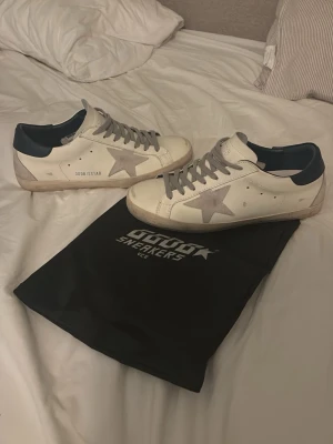 Golden goose skor äkta - Golden Goose sneakers i vitt läder med grå stjärndetalj på sidan, grå skosnören och mörkblå häl. Klassisk låg modell med slitna detaljer för en cool och avslappnad look. Perfekta för dig som gillar streetstyle och premiumkänsla.