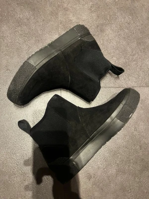 Svarta Chelsea boots från Tretorn - Säljer ett par svarta Chelsea boots från Tretorn med stretchig ovandel och robust sula. Skorna har dragflik bak och är tillverkade i en mix av textil och mocka. Snygg, minimalistisk design som passar till det mesta.