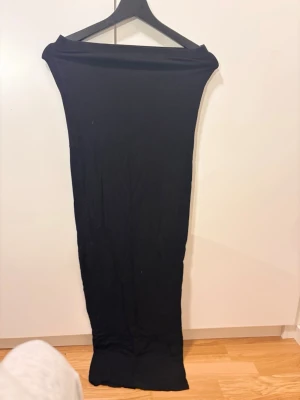 Svart lång tight kjol - En svart, lång och tight kjol i stretchigt material. Kjolen har en enkel och stilren design utan synliga detaljer eller mönster. Perfekt för dig som gillar minimalistisk stil och vill ha en kjol som sitter snyggt längs kroppen.