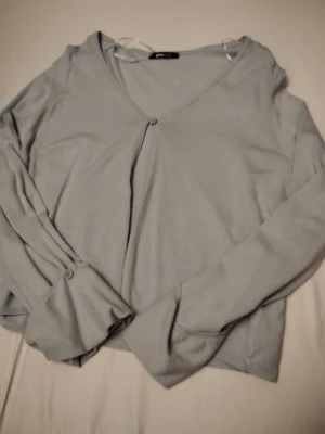 Ljusblå cardigan från Gina Tricot - (NY UTAN PRISLAPP)Snygg ljusblå cardigan från Gina Tricot med v-ringning och knappstängning framtill. Långärmad modell i mjukt, tunt material som passar perfekt till lager på lager. Enkel och stilren design med ribbade muddar och knappdetalj vid ärmslut.