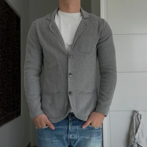 Grå stickad kavaj  - Snygg grå stickad kavaj från Seidensticker i storlek M. Kavajen har tre knappar framtill, tre fickor och en mjuk, strukturerad stickad känsla. Perfekt för en chill men ändå uppklädd look. Passformen är normal och den har långa ärmar.