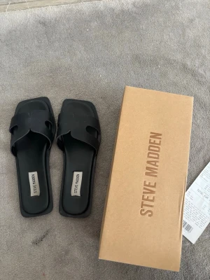 Svarta sandaler från Steve Madden - Säljer ett par svarta sandaler från Steve Madden perfekt för sommaren!💞 med öppen tå och trendig fyrkantig sula. Ovandelen är i slätt konstläder med snygga utskärningar. Perfekta för dig som gillar minimalistisk och stilren design.