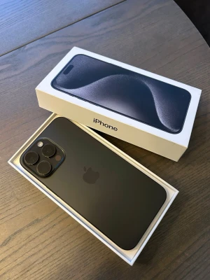 iPhone 15 Pro Max svart titan - Säljer en iPhone 15 Pro Max i snygg svart titan med stilren design och rundade kanter. Baksidan är matt och mobilen har tre stora kameror för grymma bilder. Levereras i originalkartong. 