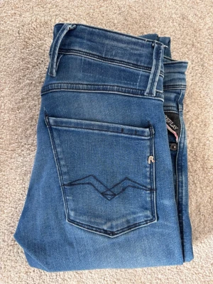 Replay Anbass - Snygga blå slim jeans från Replay med klassisk femficksdesign och diskret slitning på låren. Jeansen har en mörkblå tvätt. Storlek 28/32