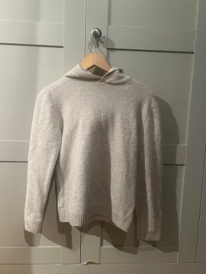 Ljusgrå hoodie i mjukt material - En stilren ljusgrå hoodie med huva och ribbade muddar vid ärmslut och nederkant. Hoodien har en enkel design utan tryck eller logga och är gjord i ett mjukt, stickat material som känns skönt mot huden. Perfekt för dig som gillar en clean och avslappnad look. Denna är från HM.