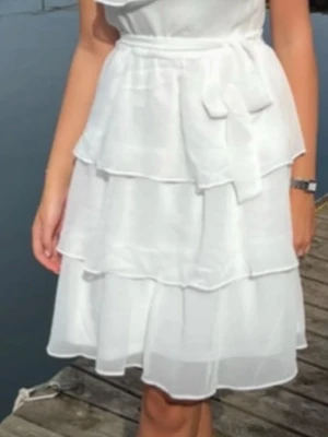 Vit student  omlottklänning med volanger - Söt vit klänning med omlottdesign och volanger i flera lager. Klänningen har ett knytband i midjan och är tillverkad i ett lätt, luftigt material som passar perfekt för varma dagar och studenter. 