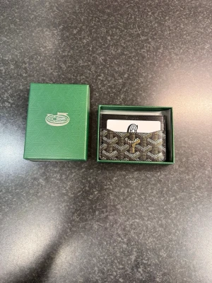 Svart korthållare  - Snygg svart korthållare  med klassiskt mönster i vitt och grått. Tillverkad i läder med flera fack för kort. Kommer i original grön ask med logga. Perfekt för dig som vill ha en stilren och exklusiv accessoar.