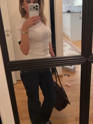 Vit Zara T-shirt  - Säljer en stilren vit t-shirt med svarta detaljer vid ärmsluten. T-shirten har en klassisk passform och är kortärmad, perfekt till jeans eller kjol. Materialet känns mjukt och bekvämt.