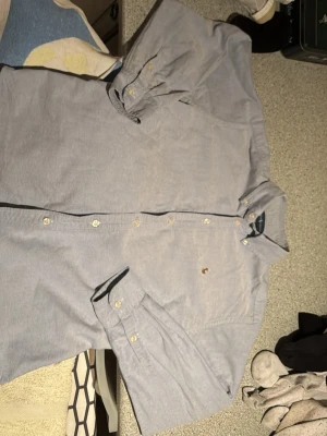 Ljusblå skjorta från Ralph Lauren - Klassisk ljusblå skjorta från Ralph Lauren med button-down krage och broderad logga på bröstet. Skjortan har långa ärmar, vita knappar och är tillverkad i mjuk bomull. Perfekt för en clean och stilren look.