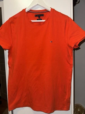 Orange t-shirt från Tommy Hilfiger - Snygg orange t-shirt från Tommy Hilfiger med liten broderad logga på bröstet. Modellen är extra slim fit och har rund halsringning samt korta ärmar. Tillverkad i mjuk bomull som känns skön mot huden.