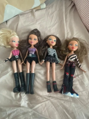 Fyra Bratz dockor med coola outfits - Säljer fyra Bratz dockor med olika outfits. Dockorna har kläder i svart, lila, rosa och ränder samt höga stövlar och byxor med detaljer. Perfekt för dig som gillar att styla och samla Bratz. Alla dockor har långt hår och unika kläder. Bra skick! Samlarobjekt 