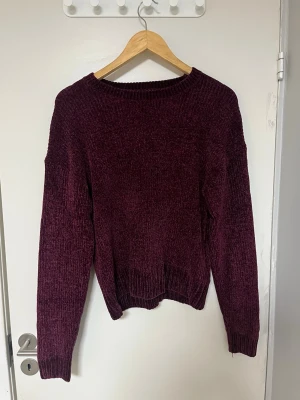 Vinröd chenilletröja med rund hals - Mysig vinröd stickad tröja i mjukt chenillematerial. Tröjan har rund halsringning, långa ärmar och ribbade muddar vid ärmslut och nederkant. Perfekt för kalla dagar och enkel att matcha till olika outfits. Mer lila färg.