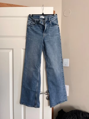 Blåa raka jeans från perfekt jeans  - Säljer ett par ljusblå jeans med hög midja och raka, vida ben. Klassisk femficksmodell i slitstark denim med dragkedjegylf och knapp. Perfekta för en avslappnad och trendig look.