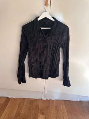 Svart plisserad skjorta från Monki - Snygg svart skjorta från Monki i plisserat material. Storlek 34. Knappt använt 