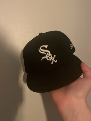 Svart New Era White Sox keps - Snygg svart keps från New Era med Chicago White Sox-logga broderad i vitt framtill. Klassisk rak skärm och broderad MLB-logga bak. Perfekt för dig som gillar streetwear och sportig stil. Använd ett fåtal gånger nypris 500