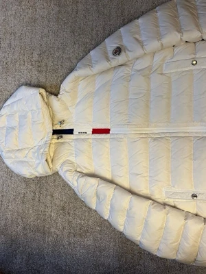 Vit dunjacka från Moncler med huva - Säljer en vit Moncler dunjacka i mycket fint skick. Knappt använd och fortfarande fräsch, helt ren utan några synliga tecken på slitage. Sitter riktigt bra på kroppen och är varm utan att kännas tung eller klumpig:) Dragkedja, knappar och logga är i toppskick, och helhetskänslan är nära nyskick. Perfekt om du vill ha en stilren och pålitlig vinterjacka till ett bra pris, som du inte kan hitta på butik! 