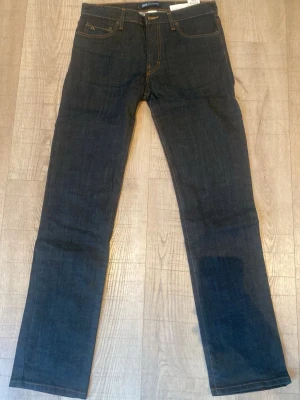 Mörkblå jeans från J.Lindeberg - Snygga mörkblå jeans från J.Lindeberg med raka ben och klassisk femficksmodell. Jeansen har kontrastsömmar i gult och diskret JL-logga på myntfickan. Tillverkade i ett mjukt och slitstarkt denimtyg som passar perfekt till din vardagsstil.