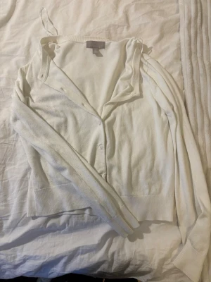 Vit tunn kofta med knappar - Enkel och stilren vit kofta med knäppning framtill. Koftan har långa ärmar, ribbade muddar och är tillverkad i ett tunt, mjukt material som passar perfekt för lager på lager. Klassisk och lättmatchad modell. Köpt på HM för lite över ett år sedan, använd ksk 10 ggr💗